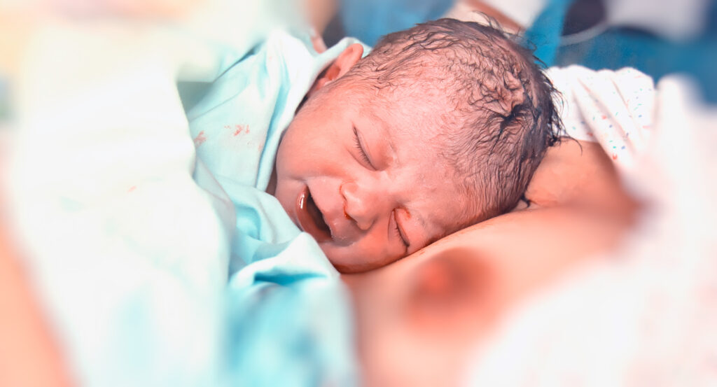 Neugeborenes liegt nach der Geburt auf der Brust der Mutter