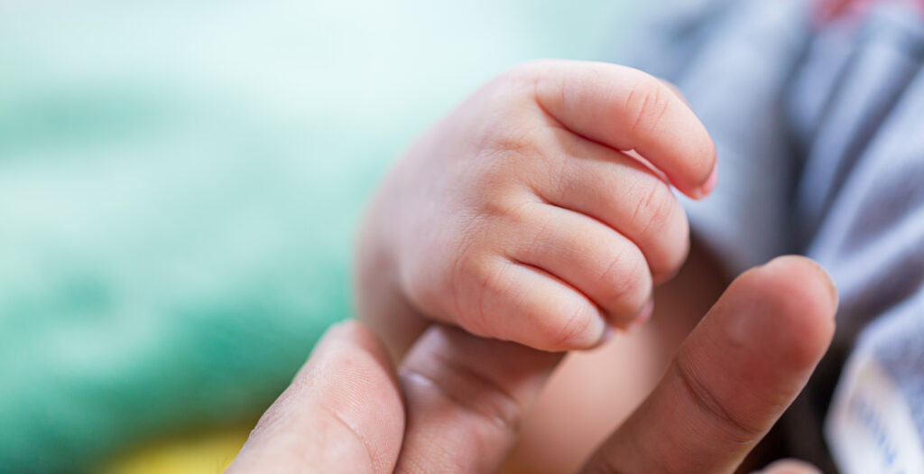 Babyhand hält den Finger eines Erwachsenen – Begleitung durch die Familienhebamme